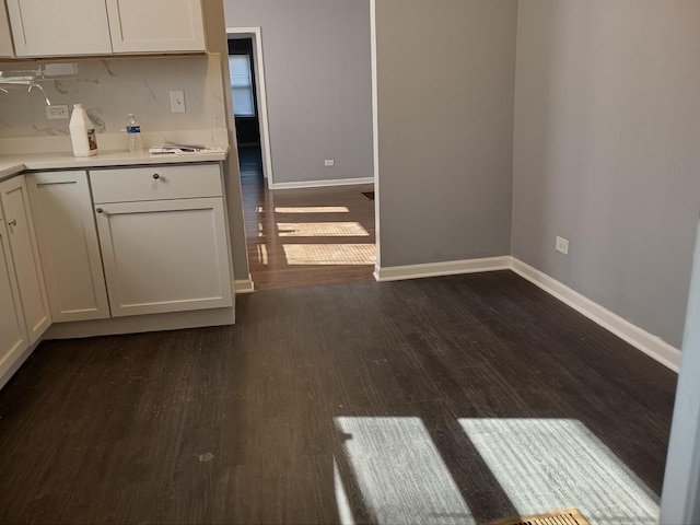 kitchen featuring light countertops, dark wood finished floors, baseboards, and white cabinetry