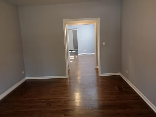 spare room with dark wood-style floors, visible vents, and baseboards