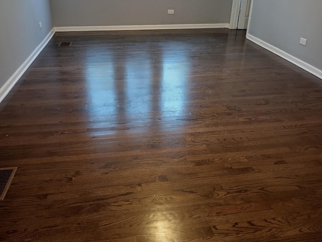 spare room with dark wood-style flooring, visible vents, and baseboards