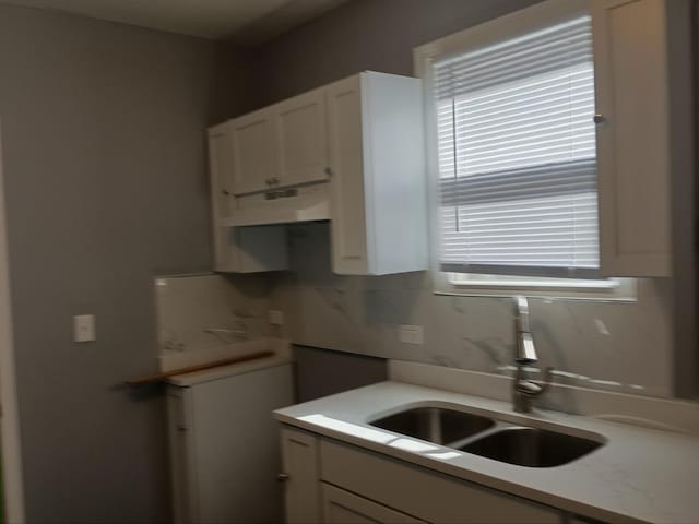 kitchen with tasteful backsplash, white cabinets, a sink, and light countertops