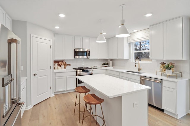 kitchen with light wood finished floors, white cabinets, a kitchen island, appliances with stainless steel finishes, and a sink