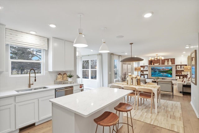 kitchen with light wood-type flooring, stainless steel dishwasher, open floor plan, and a sink