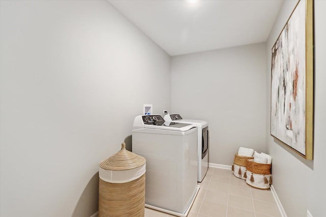 washroom featuring laundry area, washing machine and dryer, light tile patterned floors, and baseboards