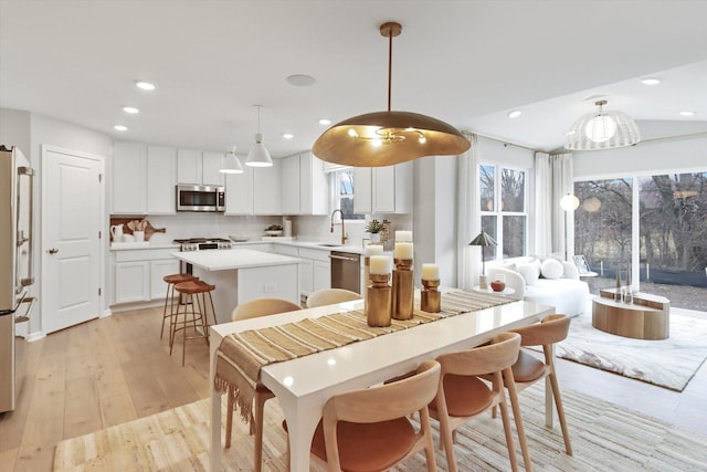 kitchen with white cabinets, light wood-style flooring, a kitchen island, a breakfast bar, and stainless steel appliances