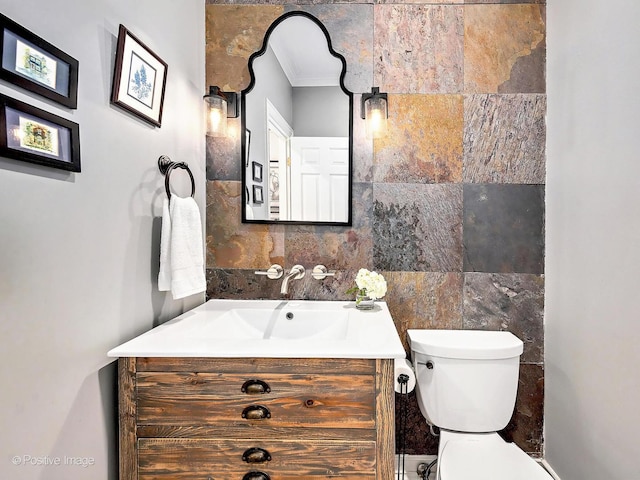 half bathroom featuring vanity, crown molding, tile walls, toilet, and backsplash