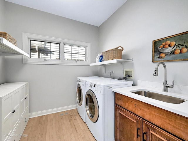 laundry area with baseboards, light wood finished floors, cabinet space, a sink, and independent washer and dryer