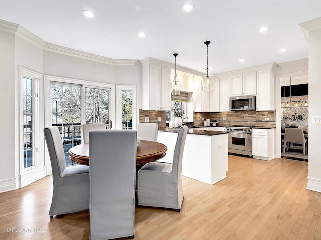 kitchen featuring dark countertops, light wood finished floors, ornamental molding, white cabinets, and stainless steel appliances