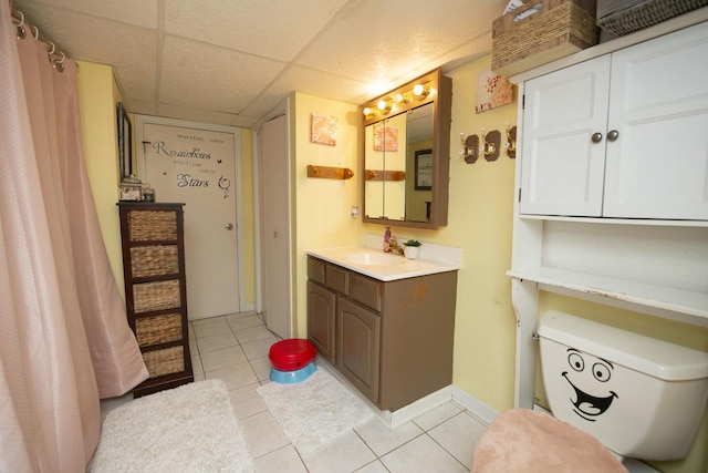 bathroom with a drop ceiling, tile patterned flooring, toilet, vanity, and baseboards