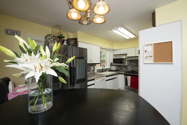 kitchen with tasteful backsplash, dark countertops, appliances with stainless steel finishes, white cabinets, and a sink