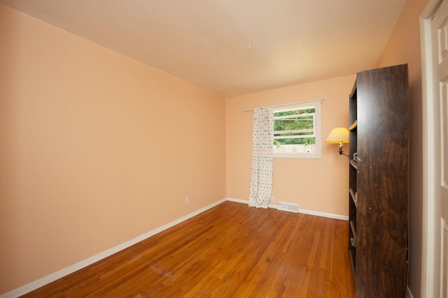 spare room with baseboards, visible vents, and wood finished floors