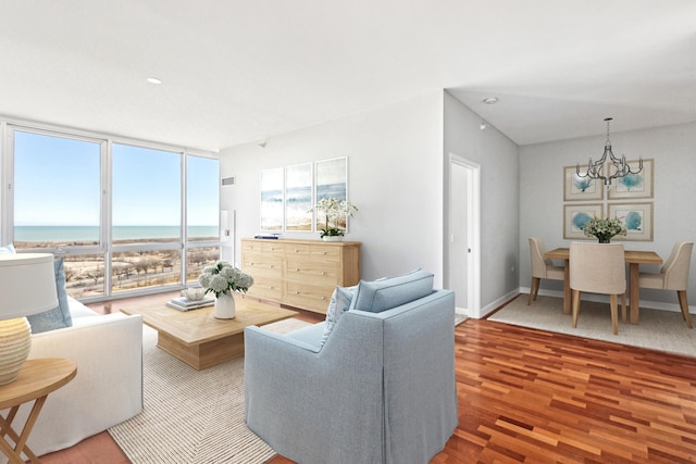 living room featuring baseboards, wood finished floors, a water view, an inviting chandelier, and floor to ceiling windows