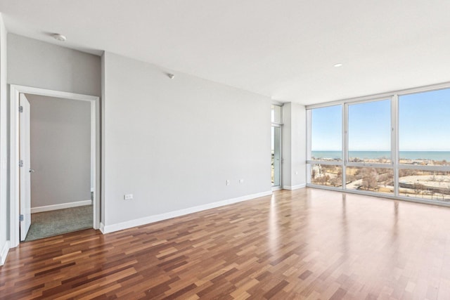 empty room with a water view, baseboards, a wall of windows, and wood finished floors