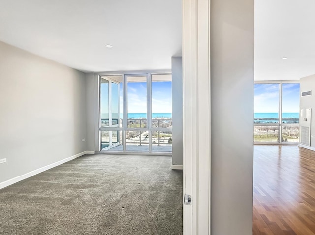 carpeted spare room with expansive windows, a water view, visible vents, and baseboards