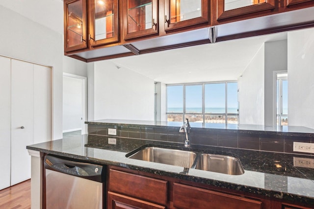 kitchen featuring stainless steel dishwasher, glass insert cabinets, a sink, dark stone countertops, and wood finished floors