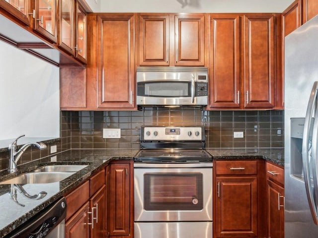 kitchen featuring backsplash, appliances with stainless steel finishes, glass insert cabinets, a sink, and dark stone countertops