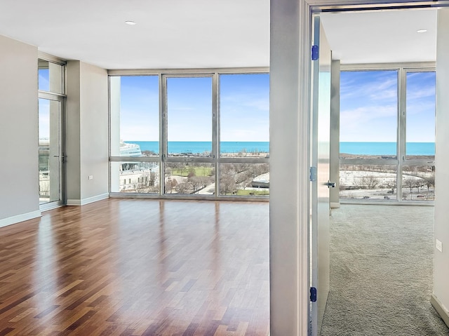 interior space with a wall of windows, a water view, wood finished floors, and baseboards