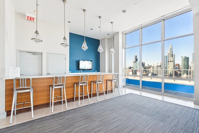 kitchen with pendant lighting, a high ceiling, a wall of windows, tile patterned flooring, and a kitchen bar