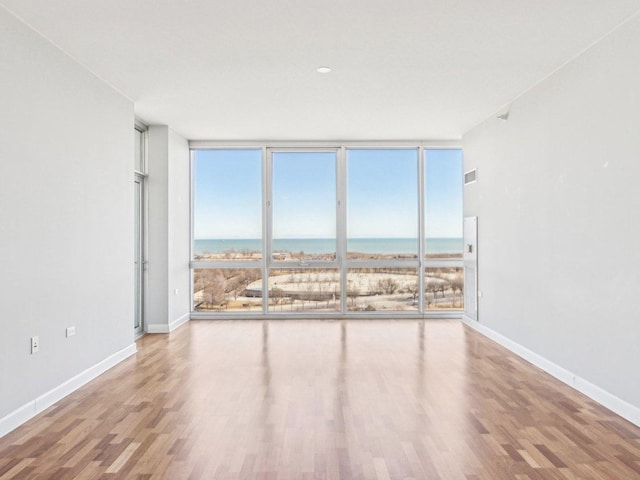 empty room with expansive windows, a water view, baseboards, and wood finished floors