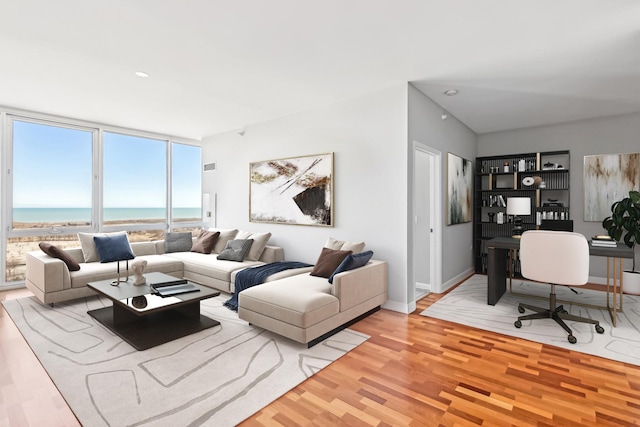 living area featuring light wood-style floors, floor to ceiling windows, a water view, and baseboards