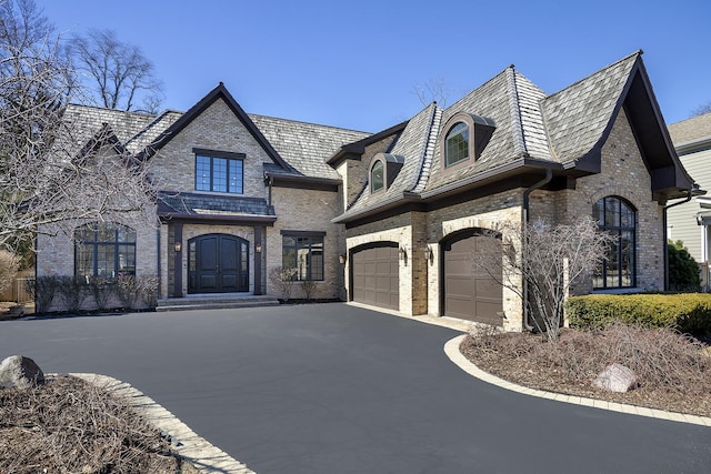 french country home with brick siding, an attached garage, and driveway