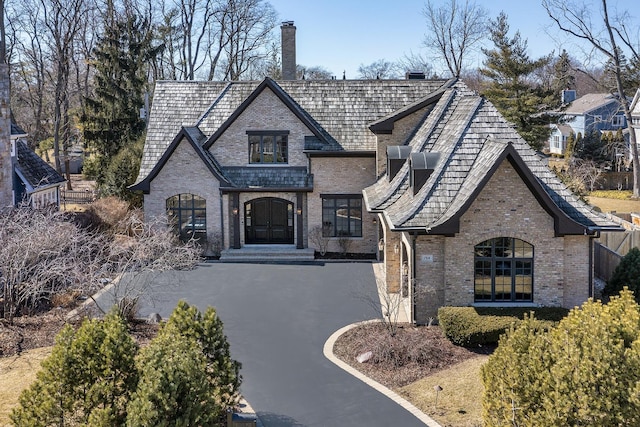 french country style house with brick siding, a chimney, and aphalt driveway