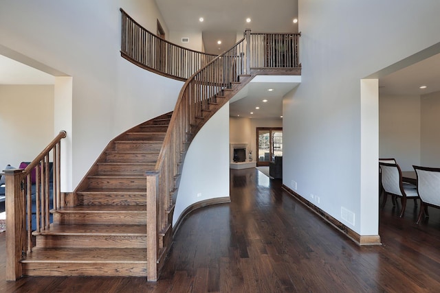 stairs featuring baseboards, a high ceiling, a fireplace with raised hearth, and wood finished floors