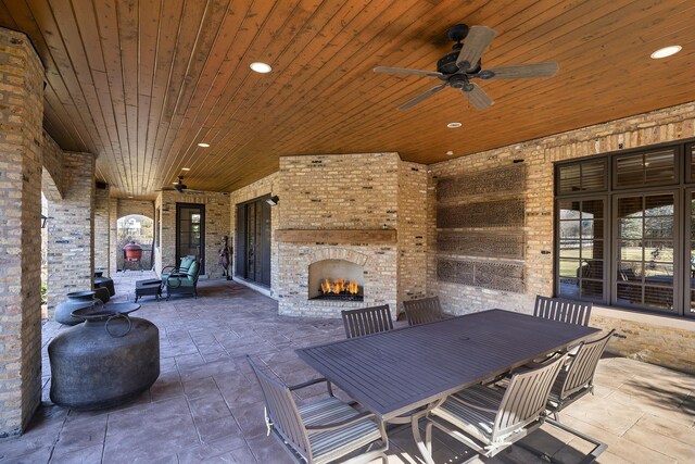 view of patio / terrace with outdoor dining area, a ceiling fan, and an outdoor brick fireplace