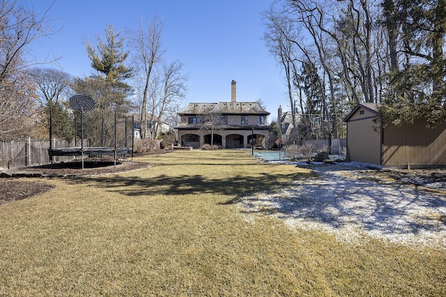 view of yard featuring an outbuilding, a trampoline, a storage shed, and fence