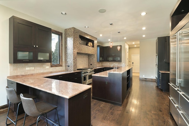 kitchen featuring dark wood-type flooring, a center island with sink, double oven range, backsplash, and a peninsula