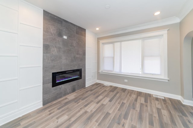 unfurnished living room with arched walkways, a tile fireplace, wood finished floors, baseboards, and crown molding