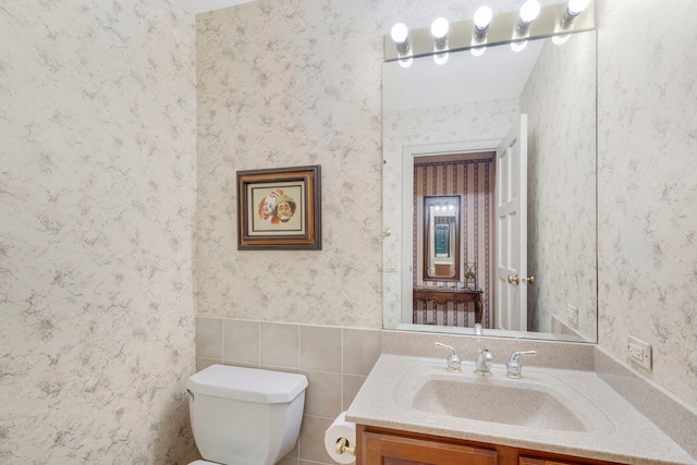 bathroom featuring a wainscoted wall, toilet, vanity, and wallpapered walls