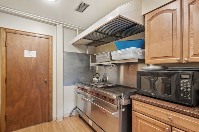 kitchen featuring dark countertops, visible vents, black microwave, range with two ovens, and exhaust hood