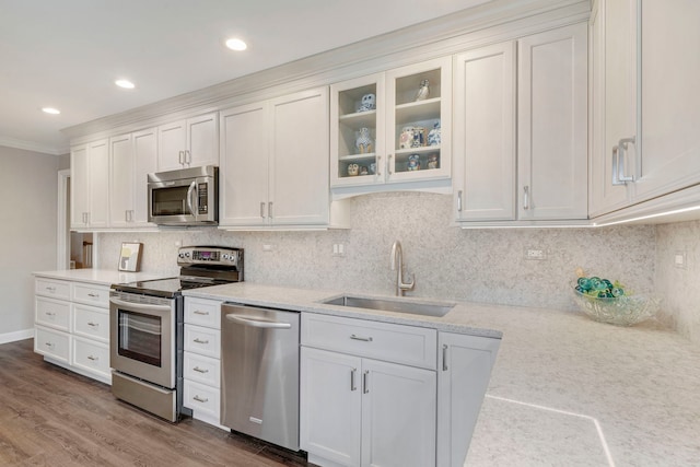 kitchen with a sink, stainless steel appliances, glass insert cabinets, white cabinetry, and tasteful backsplash