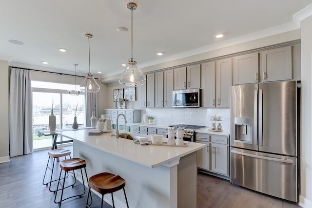 kitchen with a breakfast bar area, stainless steel appliances, gray cabinets, decorative backsplash, and a sink