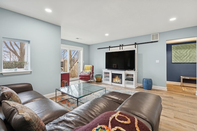 living area with visible vents, baseboards, a barn door, recessed lighting, and light wood-style floors