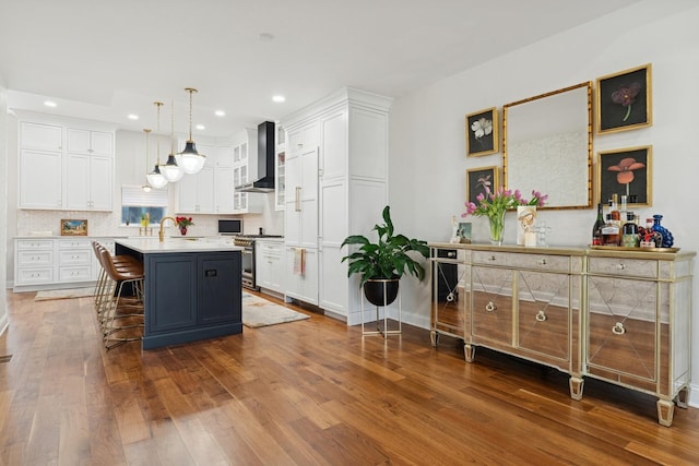 kitchen with light countertops, white cabinets, wall chimney exhaust hood, and wood finished floors