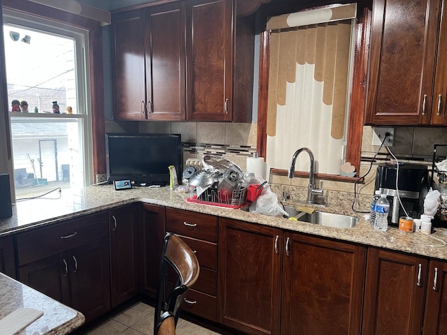 kitchen with decorative backsplash, light stone counters, a sink, a wealth of natural light, and light tile patterned flooring