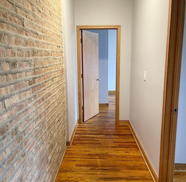 hallway featuring brick wall, wood finished floors, and baseboards