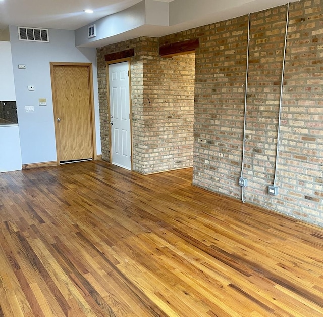 unfurnished room with brick wall, wood finished floors, visible vents, and baseboards