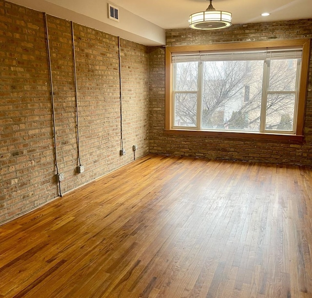 spare room featuring a wealth of natural light, visible vents, hardwood / wood-style floors, and brick wall