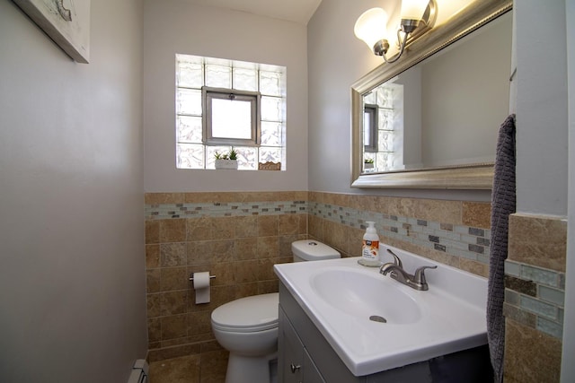 half bathroom featuring vanity, tile walls, toilet, and a wainscoted wall