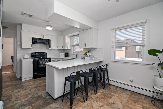 kitchen with visible vents, a breakfast bar, baseboard heating, a peninsula, and black appliances