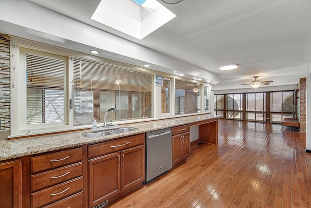 kitchen with a skylight, light wood-style flooring, brown cabinets, stainless steel dishwasher, and a sink