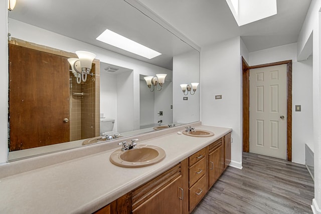 bathroom featuring wood finished floors, a skylight, a sink, and toilet