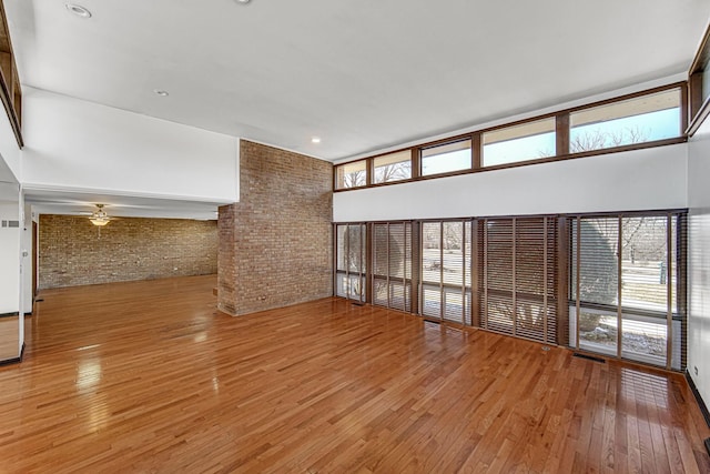 unfurnished living room featuring visible vents, brick wall, wood-type flooring, and a towering ceiling