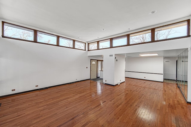 unfurnished living room with visible vents, a towering ceiling, hardwood / wood-style flooring, and baseboards