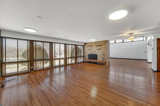 unfurnished living room featuring a ceiling fan, a wealth of natural light, a fireplace, and hardwood / wood-style floors