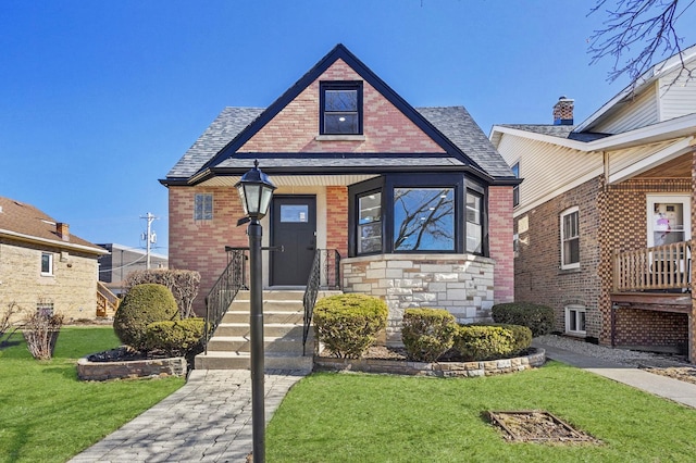 view of front of property featuring brick siding, roof with shingles, and a front yard