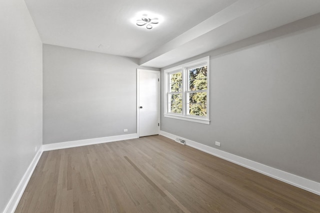 empty room featuring wood finished floors, visible vents, and baseboards