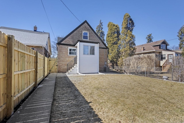 rear view of property with entry steps, brick siding, a yard, and a fenced backyard